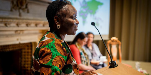 Elderly black woman with multicolored shirt speaks at a podium